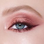 Single-eye close-up of a fair-tone model with blue eyes wearing eye makeup in shades of pearlescent rose gold, dusky rose, berry brown and rose-bud pink with berry-brown eyeliner and dark brown mascara.
