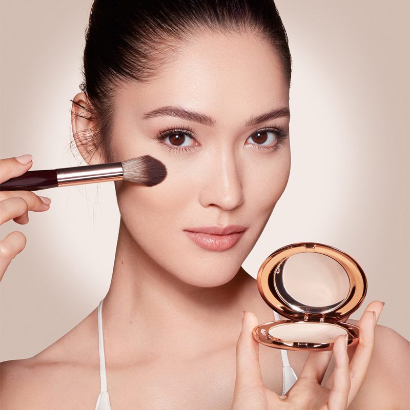 A fair-tone model wearing glowy makeup and applying a radiant, setting powder that brightens, cover blemishes, and makes her skin look fresh.