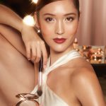 Fair-tone brunette model wearing dew makeup with smokey eye makeup, nude lipstick, and glowy powder highlighter in a silvery-gold shade.