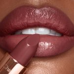 Lips close-up of a deep-tone model applying a berry-brown lipstick with a satin-finish.