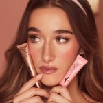 A fair skin model holding and wearing a liquid blush and liquid highligher