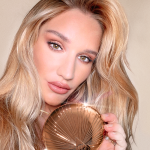 Sofia Tilbury holding a bronzer compact in dark golden packaging with a starburst pattern on the outside.