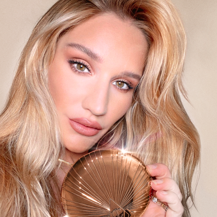 Sofia Tilbury holding a bronzer compact in dark golden packaging with a starburst pattern on the outside.