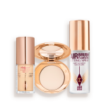 Travel-size kit that includes a glowy primer in a glass bottle with gold-coloured lid, face powder compact in a light shade with a mirrored-lid in gold-coloured packaging, and setting spray in a clear bottle with gold-coloured lid.