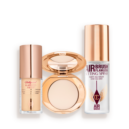 Travel-size kit that includes a glowy primer in a glass bottle with gold-coloured lid, face powder compact in a light shade with a mirrored-lid in gold-coloured packaging, and setting spray in a clear bottle with gold-coloured lid.