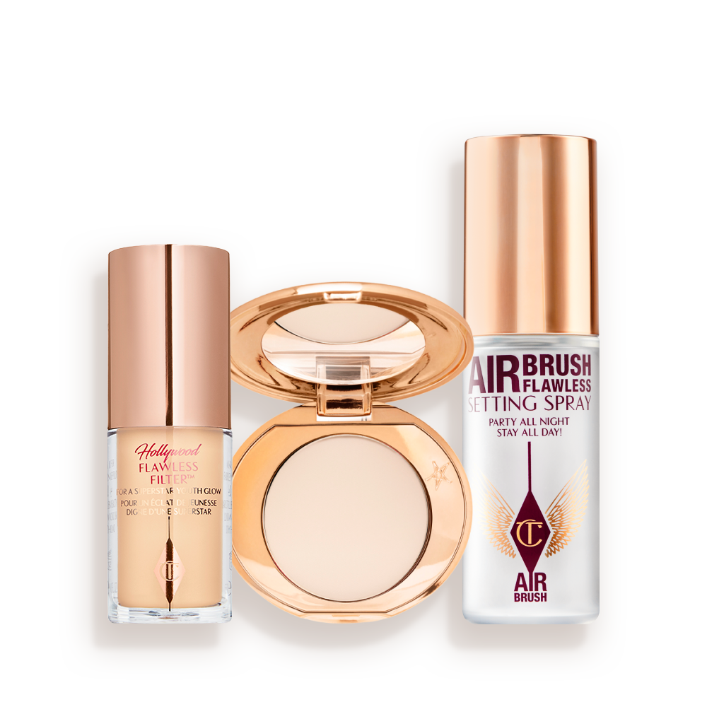 AIRBRUSH_GLOW___SET_TRAVEL_KIT_FACE_KITA__-BUNDLE Travel-size kit that includes a glowy primer in a glass bottle with gold-coloured lid, face powder compact in a light shade with a mirrored-lid in gold-coloured packaging, and setting spray in a clear bottle with gold-coloured lid.