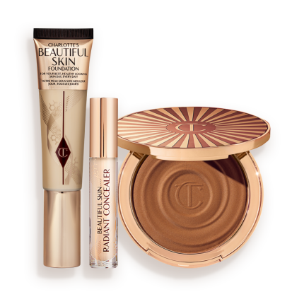 Foundation in a sleek gold-coloured tube with a concealer in a glass tube and gold-coloured lid, and dark brown cream bronzer compact in gold-coloured packaging.