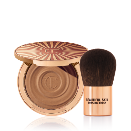 An open cream bronzer compact with gold-coloured packaging with a bronzer brush with soft,d ark-brown-coloured bristles and a golden-coloured handle.