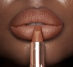 Lips close-up of a deep-tone model wearing a fresh, neutral nude peach lipstick with a matte finish.