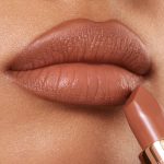 Lips close-up of a medium-tone model wearing a fresh, neutral nude peach lipstick with a matte finish.