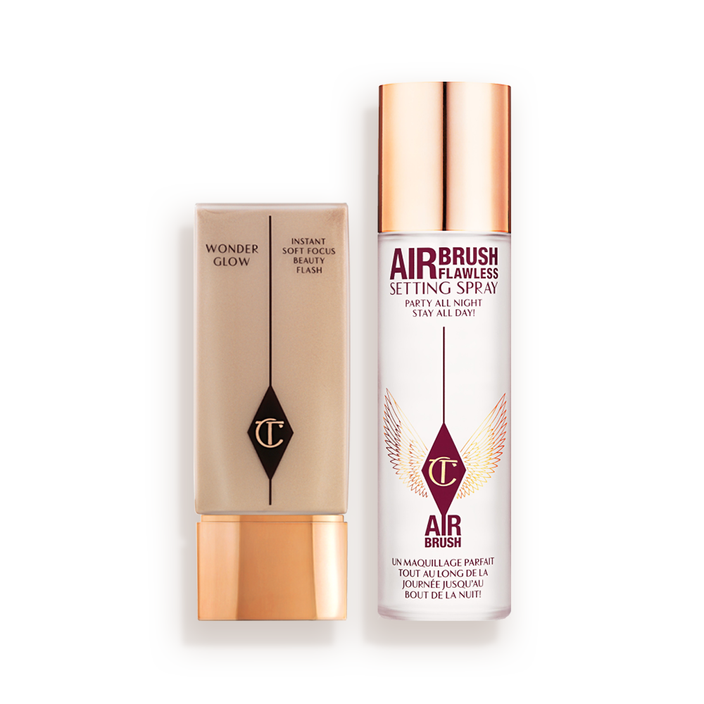 CHARLOTTEa__S_PRIME__SET___GLOW_KIT Foundation in a rectangular, clear bottle with a gold-coloured lid and setting spray in a large, clear bottle with a gold-coloured lid.