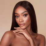 A deep-tone brunette model with glowy, face base wearing smokey brown eye makeup with bronzed, luminous face.