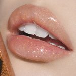 Lips close-up of a fair-tone model wearing sheer gold lip gloss with a high-shine finish.