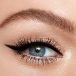 Single eye close-up of a fair-tone model with blue eyes wearing a duo eyeliner in black and champagne-beige on her upper lid and lower waterline.