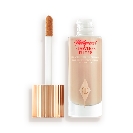 An open, luminous primer in a light cool-toned-beige shade in a glass bottle with its gold and white doe-foot applicator next to it.