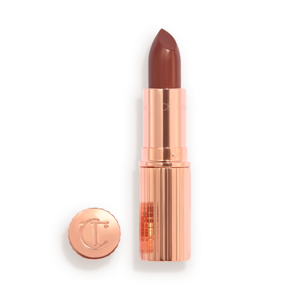 Opened, berry-pink lipstick in a metallic, golden case with its lid that's embossed with CT placed next to it.