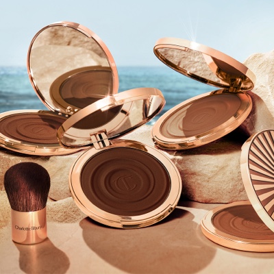 Four, open cream bronzer compacts with mirrored lids in light brown, medium brown, dark brown, and black-brown shades with gold-coloured bodies and lids.