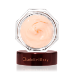 A thick and luscious dark champagne-coloured face cream in an open glass jar with a black and gold coloured lid next to it.