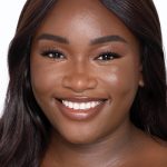 Deep-tone brunette model with brown eyes wearing nude pink lipstick with a skin-like foundation with a flawless, dewy finish.