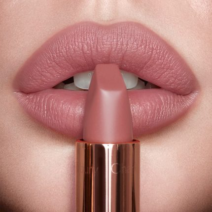 Lips close-up of a model wearing a matte, nude pink lipstick while holding the lipstick in front of her lips.