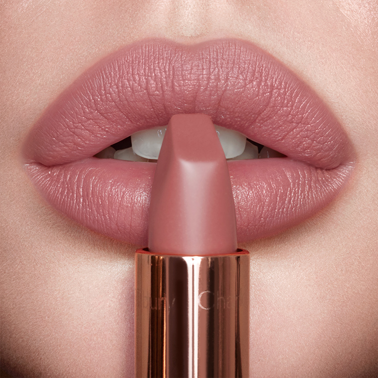 PILLOW_TALK_LIP_slick Lips close-up of a model wearing a matte, nude pink lipstick while holding the lipstick in front of her lips.
