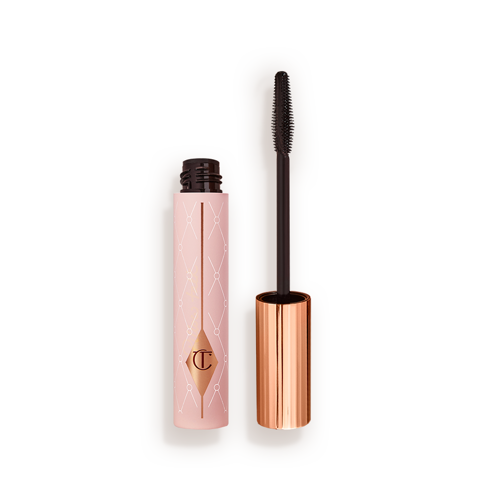 PILLOW_TALK_MASCARA_BACK_OPEN Mascara in a pink-coloured tube with its gold-coloured lid with a black applicator next to it.