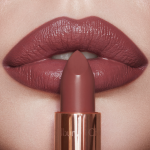 Lips close-up of a light-tone model wearing a dark, brown-pink lipstick with a satin finish while holding the lipstick in front of her.