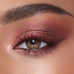 Single-eye close-up of a medium-tone model with hazel eyes wearing eye makeup in shades of pearlescent rose gold, dusky rose, berry brown and rose-bud pink,