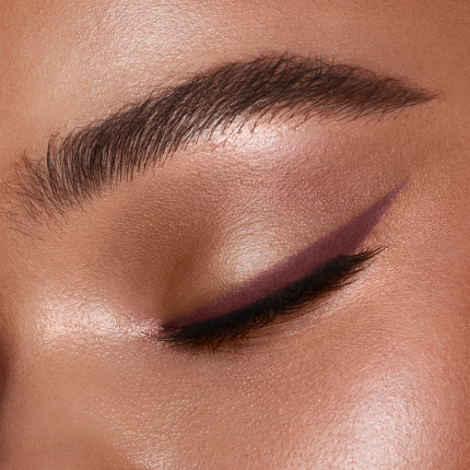 close-up of a tanned-skin model with glowing skin and groomed eyebrows with a soft winged eyeliner in berry-brown shade.