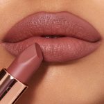 Lips closeup of a medium-tone model applying a mid-toned muted nude-rose matte lipstick.