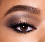 Single-eye close-up of a medium-tone model with brown eyes wearing a smokey grey, light brown, and gold eye look with black wing eyeliner.