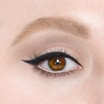 Close-up of a fair-tone model with brown eyes wearing blue-black eyeliner pencil on her eyelid and nude beige eyeliner pencil on her lower waterline.