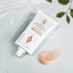 An exfoliating, wash-off, chemical mask in a white-coloured tube with gold-coloured text on it and its brown-champagne-coloured creamy swatch next to it.