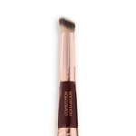 Close-up of a concealer brush with fawn and dark brown bristles with a rose-gold and dark crimson handle.