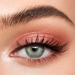 Single-eye close-up of a fair-tone model with blue eyes wearing shimmery rose gold eyeshadow.